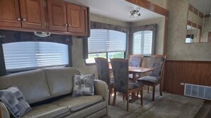Ein kompaktes Wohnmobil-Interieur mit Sofa, Esstisch, Stühlen und einer kleinen Küche.