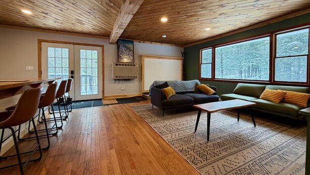 Una habitación acogedora con techo de madera, un ventanal con vistas nevadas, un sofá y una mesa de comedor con sillas.