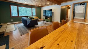 Amplia sala de estar con una gran mesa de comedor de madera, un televisor y una zona de cocina con microondas.