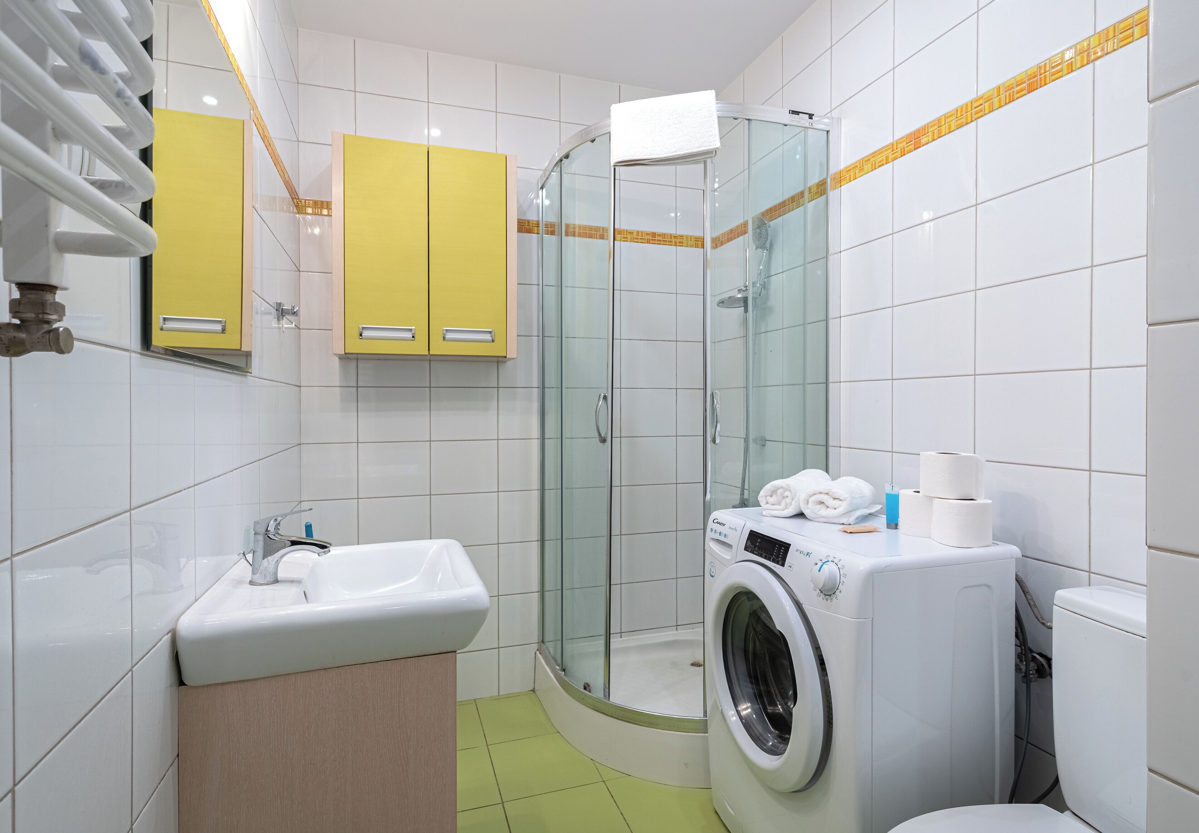 Uma casa de banho moderna com chuveiro envolto em vidro, lavatório, máquina de lavar roupa e armários amarelos.