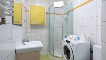 Uma casa de banho moderna com chuveiro envolto em vidro, lavatório, máquina de lavar roupa e armários amarelos.