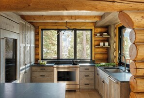 A modern kitchen with wooden cabinetry, a large window, and a built-in oven. - Skyfall Cabin | Luxury, Ski In/Out | Big Sky Resort (Big Sky)