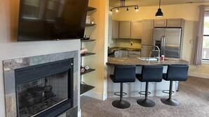 Una cocina moderna con televisor de pantalla plana, chimenea, taburetes de bar y barra.