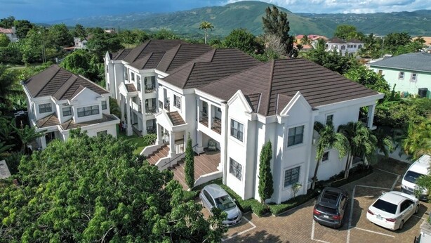A multi-story residential building with a symmetrical facade, multiple balconies, and a driveway with parked cars. - Cozy 1-bedroom apartment in perfect Mandeville with AC and gym access (Mandeville)