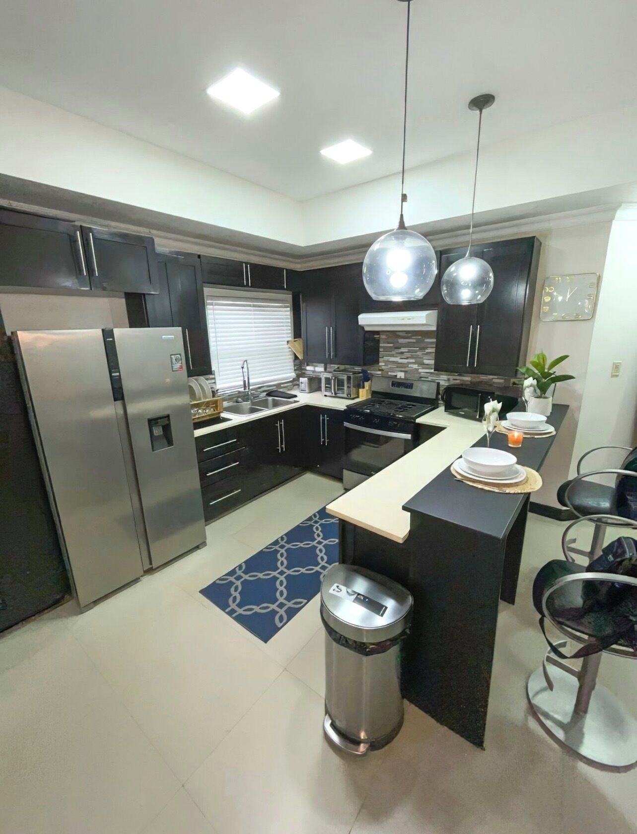 A modern kitchen with dark cabinets, stainless steel appliances, a central island with seating, and pendant lighting.