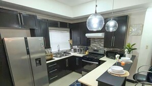 A modern kitchen with dark cabinets, stainless steel appliances, a central island with seating, and pendant lighting. - Cozy 1-bedroom apartment in perfect Mandeville with AC and gym access (Mandeville)