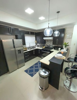 A modern kitchen with dark cabinets, stainless steel appliances, a central island with seating, and pendant lighting. - Cozy 1-bedroom apartment in perfect Mandeville with AC and gym access (Mandeville)