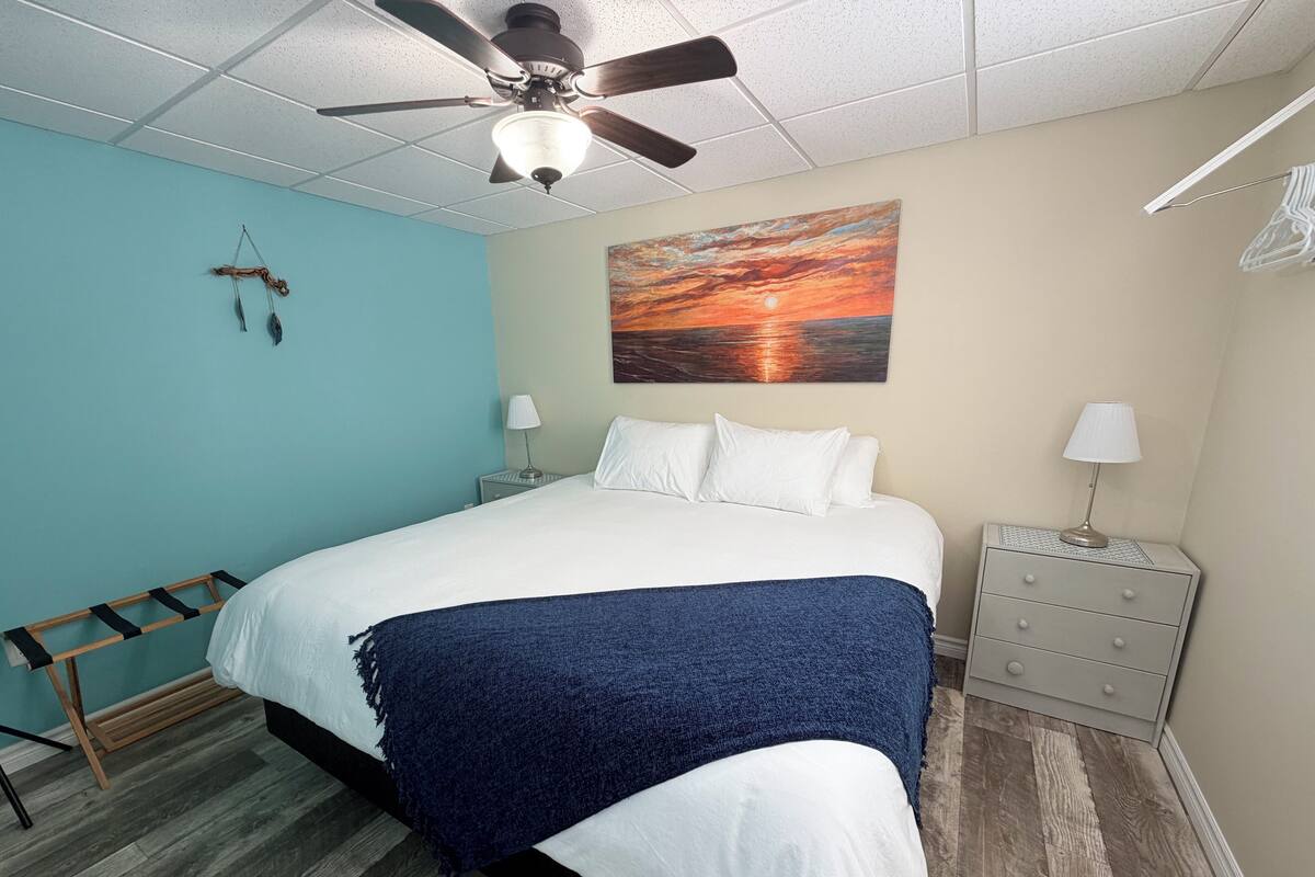 Une chambre à coucher avec un lit, un ventilateur de plafond, une table de chevet, une lampe, un tableau et une échelle en bois.