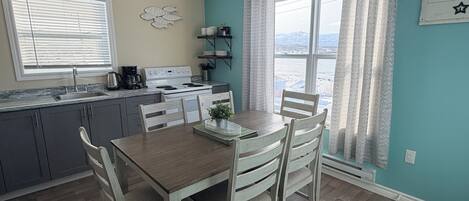Cocina compacta con comedor, que incluye una mesa y sillas de madera, horno empotrado y una ventana con cortinas estampadas.