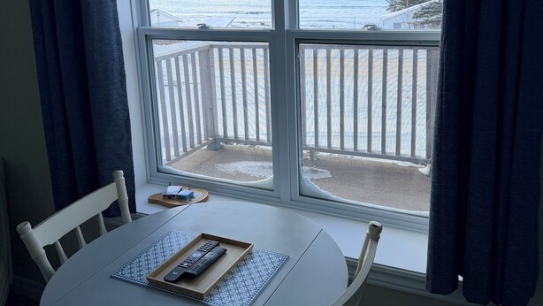 Een kamer met een ronde tafel en stoelen, een raam met uitzicht op een besneeerd landschap en een wateroppervlak.