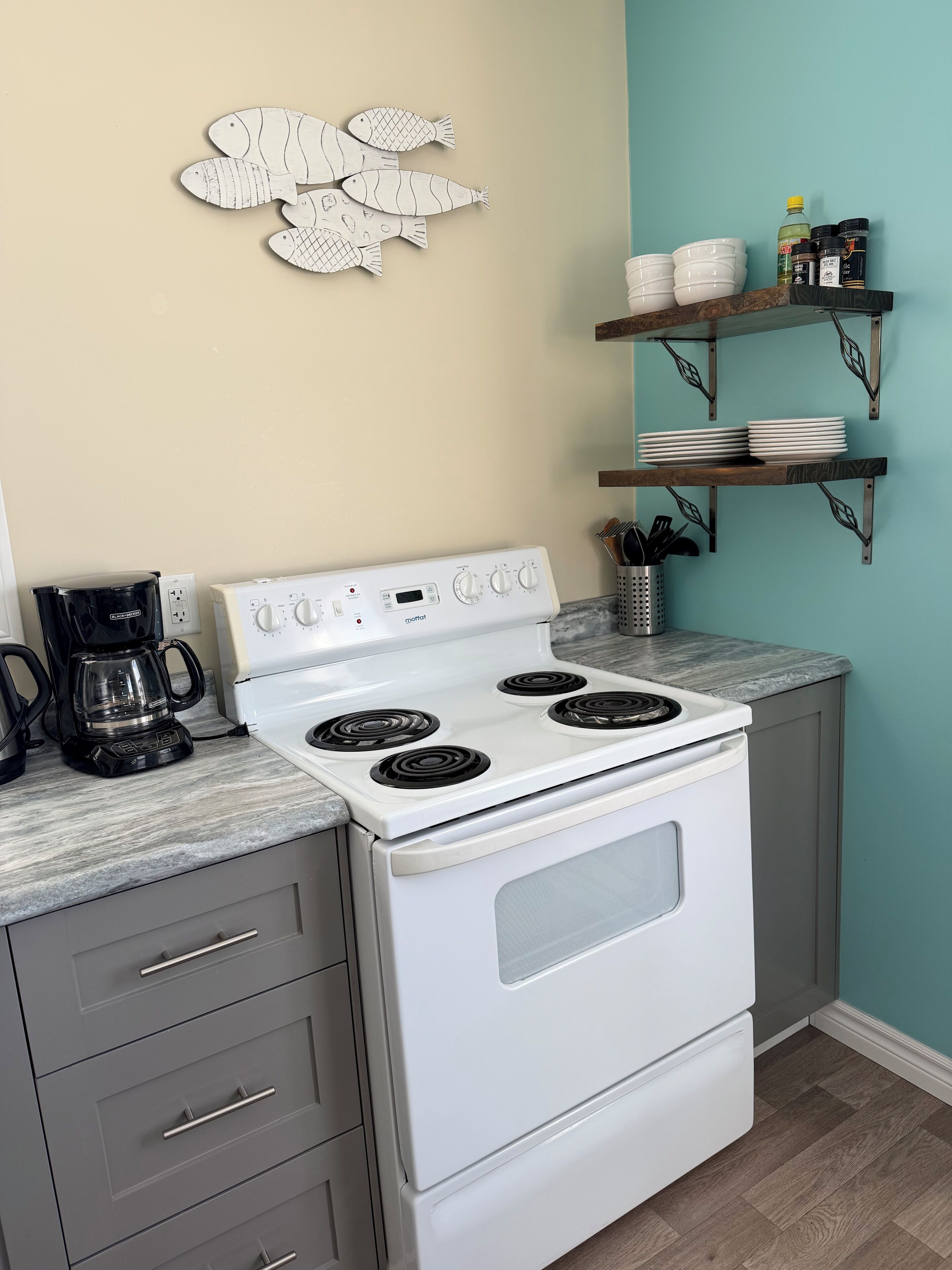 A kitchen with a white stove, a coffee maker, and a wall art piece.