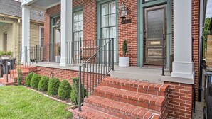 A brick house with a front porch, a green door, and a small garden.