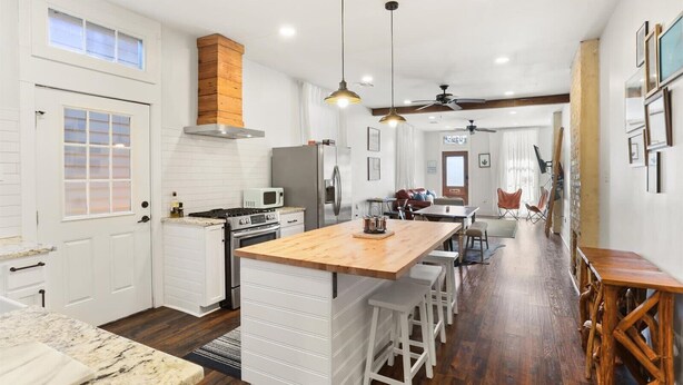 A modern kitchen with white cabinetry, a wooden island, and a dining area with bar stools.