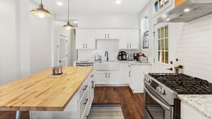 A modern kitchen with white cabinets, a wooden island, a gas stove, and pendant lighting.