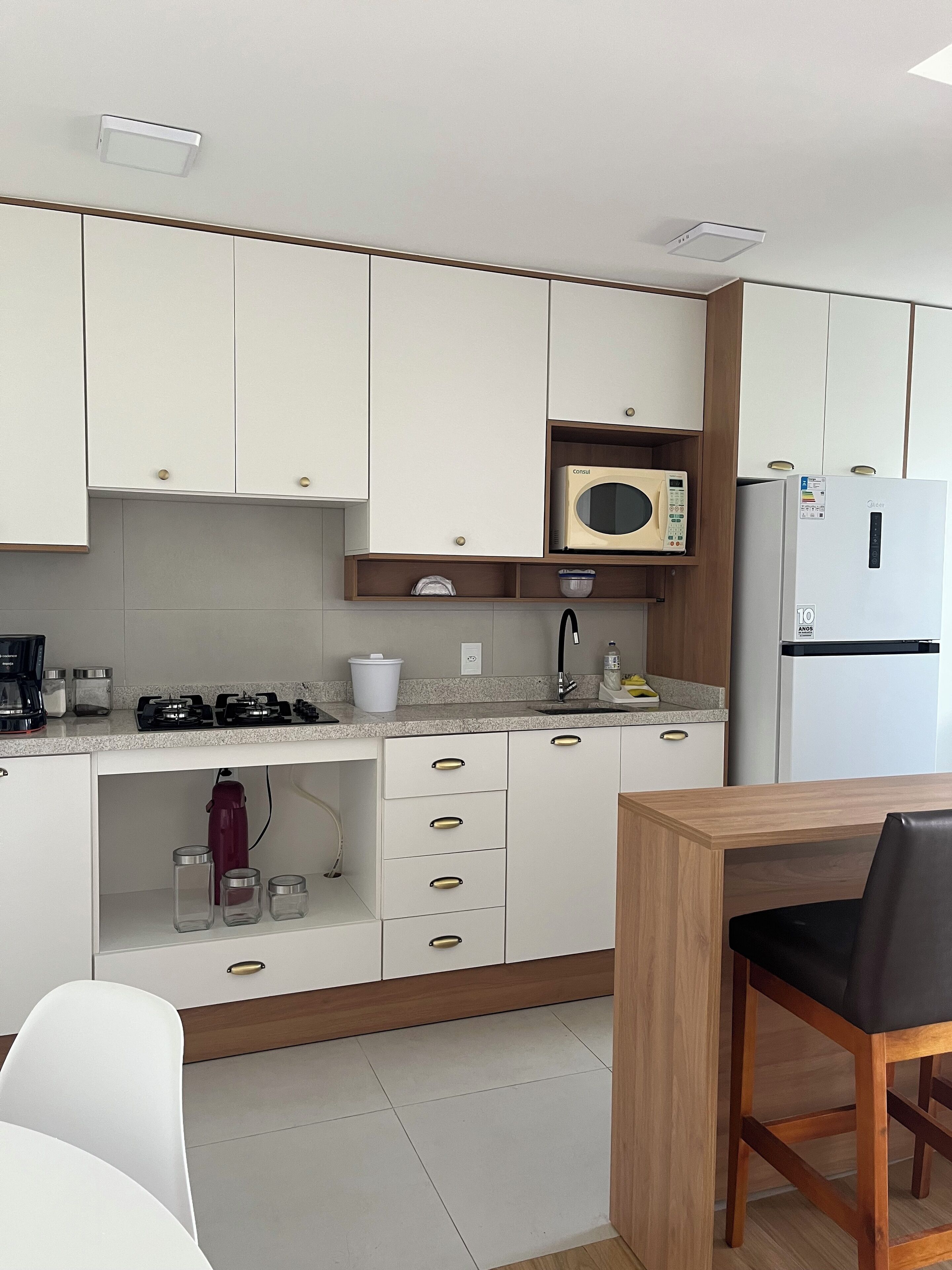 Una cuina moderna amb armaris blancs, un microones, un frigorífic, una rentavaixelles i una zona de menjador amb taula i cadires.