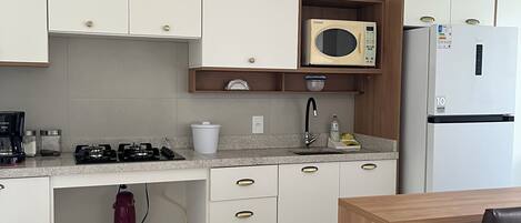 Una cocina moderna con armarios blancos, microondas, refrigerador, lavaplatos y un comedor con mesa y sillas.