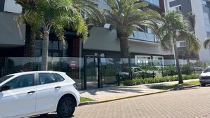 A modern building with multiple floors, glass windows, and a paved entrance area with palm trees.