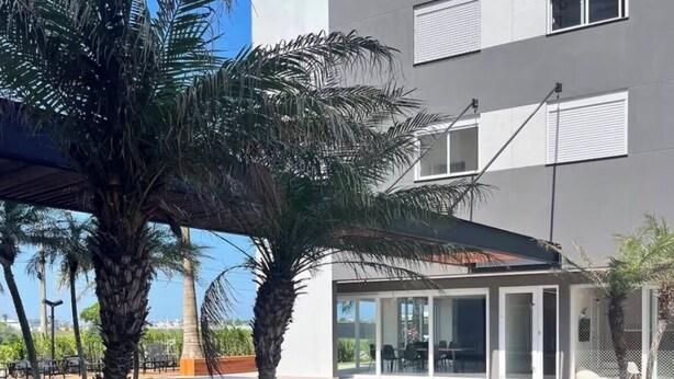 A modern building with a pool area, palm trees, and a clear blue sky.