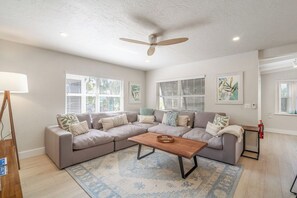 A living room with a sectional sofa, a coffee table, and a ceiling fan. - Yacht Rock Ranch (Holmes Beach)