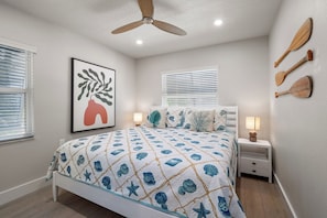 A bedroom with a bed, bedside tables, a ceiling fan, wall-mounted lamps, and a framed artwork. - Yacht Rock Ranch (Holmes Beach)