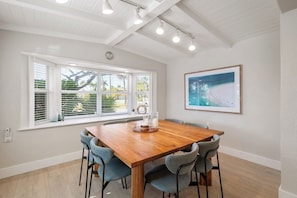 A dining area with a wooden table and four chairs, a large window with blinds, and a framed picture on the wall. - Yacht Rock Ranch (Holmes Beach)