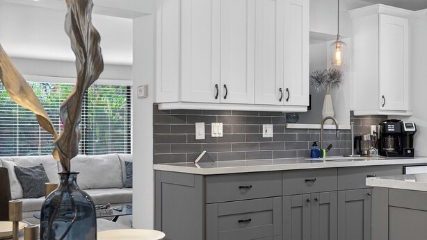A modern kitchen with white cabinets, a dark countertop, and a vase with a tall plant. - Bliss - Tropical Paradise with Heated Pool (Wilton Manors)