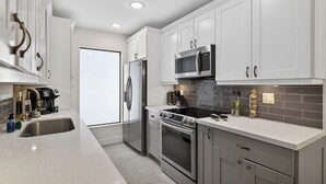 A modern kitchen with white cabinets, stainless steel appliances, and a tiled backsplash. - Bliss - Tropical Paradise with Heated Pool (Wilton Manors)