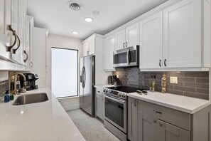 A modern kitchen with white cabinets, stainless steel appliances, and a tiled backsplash. - Bliss - Tropical Paradise with Heated Pool (Wilton Manors)