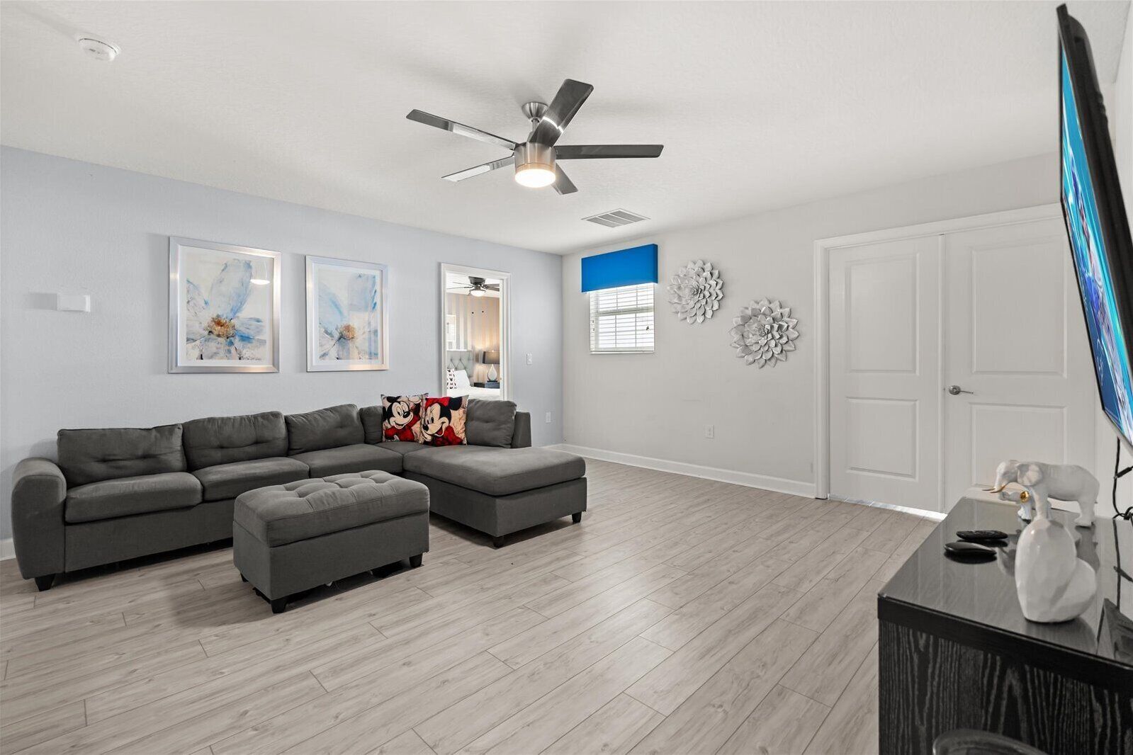 A spacious living room with a grey sectional sofa, a ceiling fan, and decorative wall art.