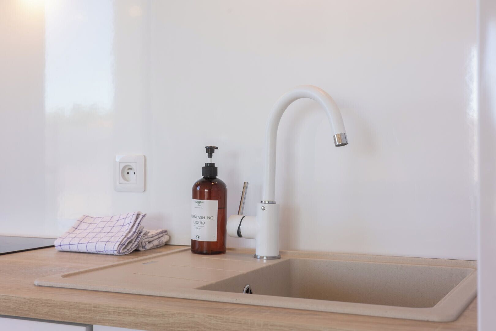 A kitchen sink with a modern faucet, a bottle of dishwashing liquid, and a towel on the counter.