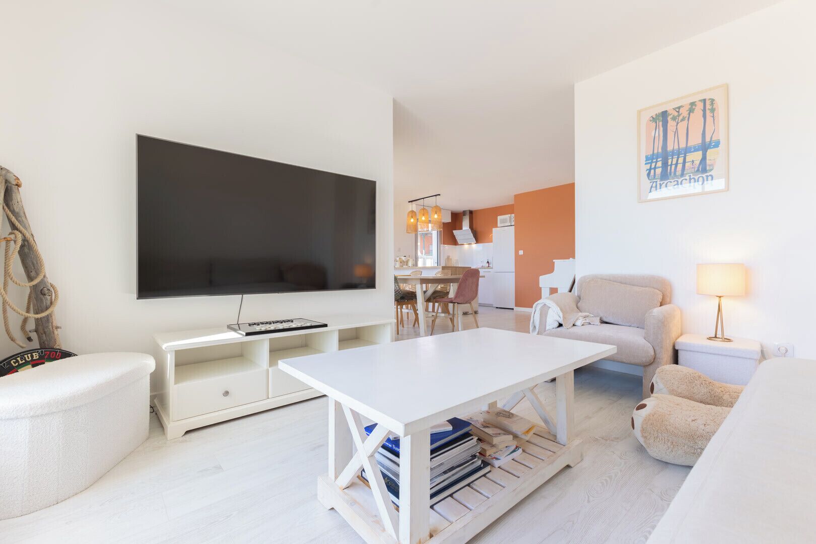A modern living room with a flat-screen TV, a dining area, and a kitchen in the background.