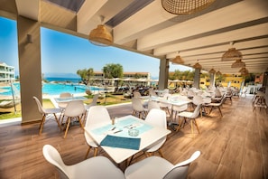 A spacious outdoor dining area with tables and chairs, overlooking a pool and the sea. - Robolla Beach (Corfu)