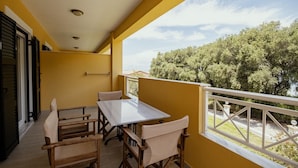 A balcony with a white table and chairs, yellow walls, and a view of trees. - Robolla Beach (Corfu)