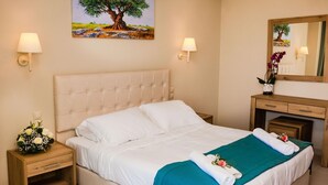 A hotel room with a large bed, a wooden nightstand with a vase of flowers, a wooden dresser, and a painting of a tree on the wall. - Robolla Beach (Corfu)