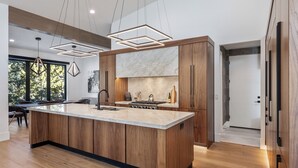 Une cuisine moderne dotée d’un grand îlot central, de meubles en bois et de luminaires suspendus.