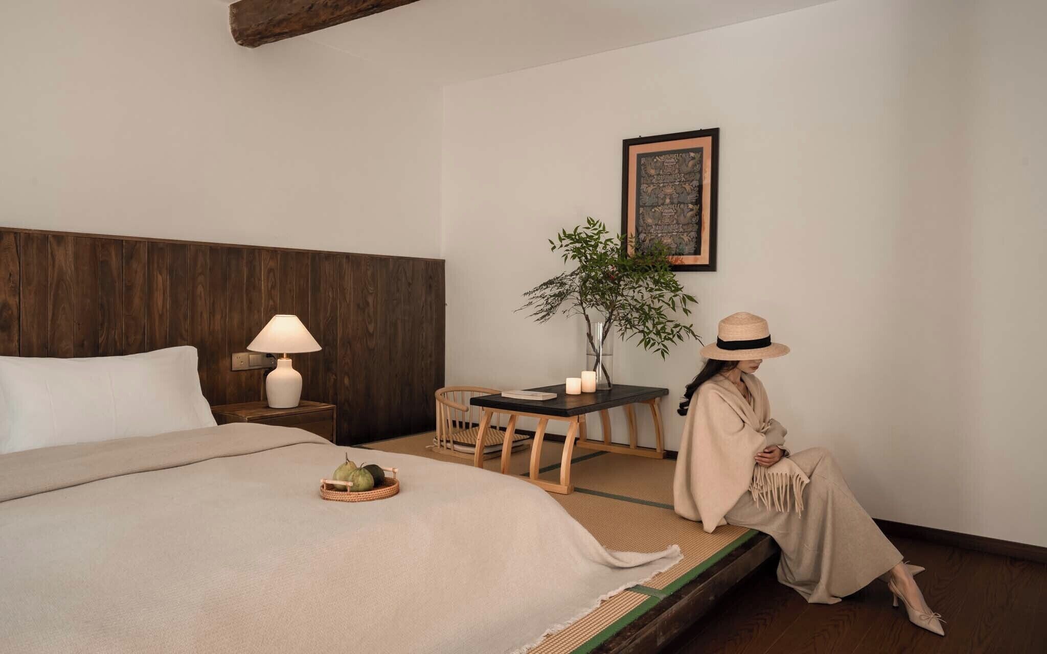 Una habitación de hotel con una cama, una mesita de noche con una lámpara, una pequeña mesa con una planta y un cuadro en la pared.
