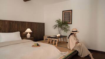 Una habitación de hotel con una cama, una mesita de noche con una lámpara, una pequeña mesa con una planta y un cuadro en la pared.