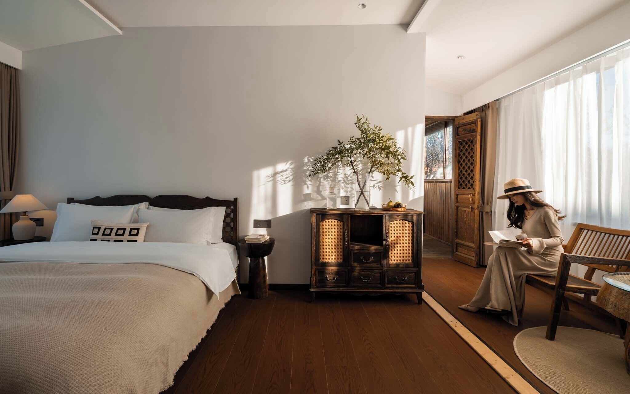 Ein Hotelzimmer mit Bett, Nachttisch, Lampe, Holzschrank und einem Fenster mit Vorhängen.