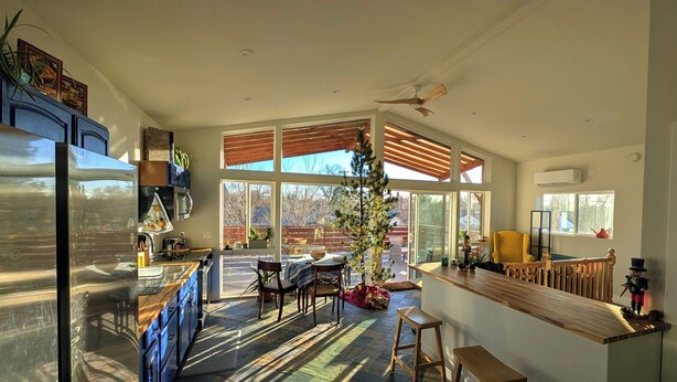 A modern kitchen with a large island, a dining area with a Christmas tree, and a view of the backyard through large windows. - Airy 1-bedroom townhome in charming Aurora with AC (Aurora)