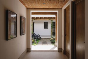 A hallway with a wooden ceiling, a door on the right, and a small garden area with steps leading to a door.