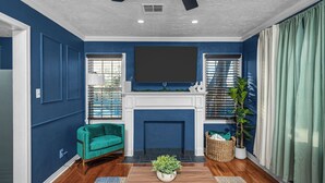 A living room with blue walls, a fireplace, a green armchair, and a ceiling fan. - Modern & Cozy Home Near Fort Sill (Lawton)