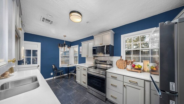A modern kitchen with white cabinets, a stainless steel refrigerator, and a black tiled floor. - Modern & Cozy Home Near Fort Sill (Lawton)