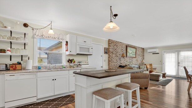 Una cocina moderna con armarios blancos, una pared decorada con ladrillo y una isla grande con taburetes.