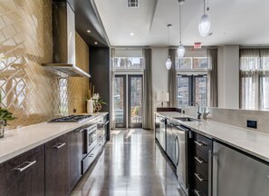 A modern kitchen with stainless steel appliances, a large island, and a view of the outdoors through large windows. - 2-bedroom apartment in the heart of La Cantera near Six Flags (San Antonio)