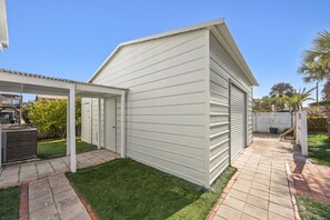 Ein eingeschossiges Gebäude mit überdachter Terrasse, kleinem Rasen und umzäunter Garten.