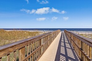 Eine Holzpromenade führt zu einem Strand unter blauem Himmel.