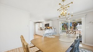 A dining area with a wooden table, wicker chairs, and a chandelier. - Newly renovated cottage! Walk to the beach! (Fernandina Beach)