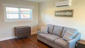 Ein Wohnzimmer mit grauem Sofa, einem Holzkabinett und einem Fenster mit Jalousien.