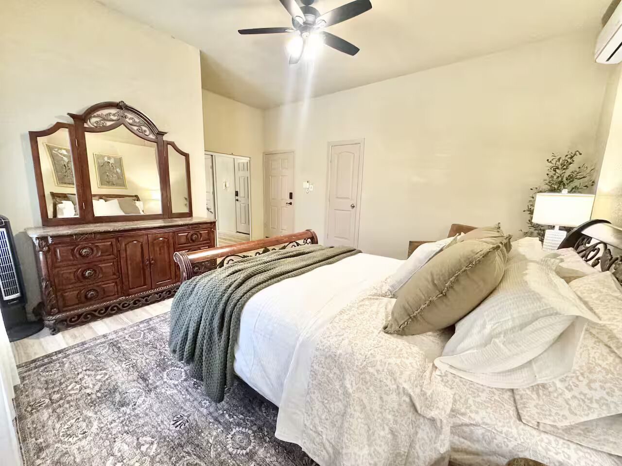 A bedroom with a bed, a dresser, a mirror, and a ceiling fan.