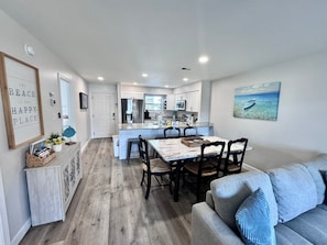 A modern kitchen with white cabinets, a stainless steel refrigerator, and a dining area with a wooden table and chairs. - Bright and modern waterfront condo in a quiet, gated community just minutes from Gulf Shores beaches (Orange Beach)